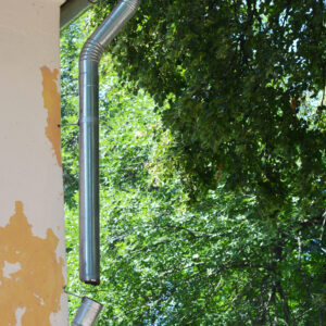 A close-up of a broken metal roof gutter, damaged downpipe, downspout of an old house that needs renovation, roof gutter to be repaired and walls to be painted.